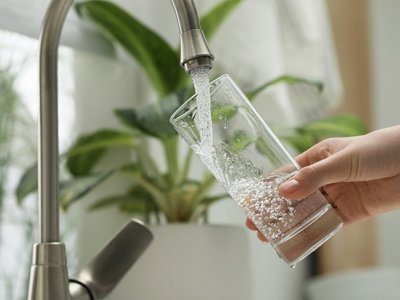 Person filling glass with water from tap. Adobe
