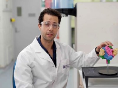 a man in a white lab coat sits next to a multicoloured model