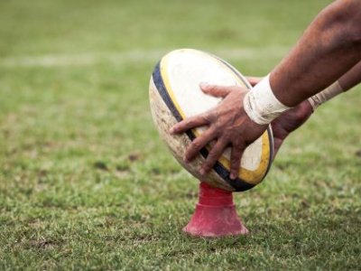 Hands holding a rugby ball on a kicking tee. 