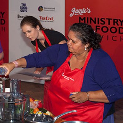 UQ student Charlotte Rashleigh assists Narrella Simpson, with Minister for Transport Rachel Nolan cooking in the background