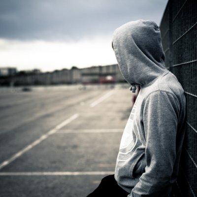 A teenager wearing a hoodie leans against a wall.