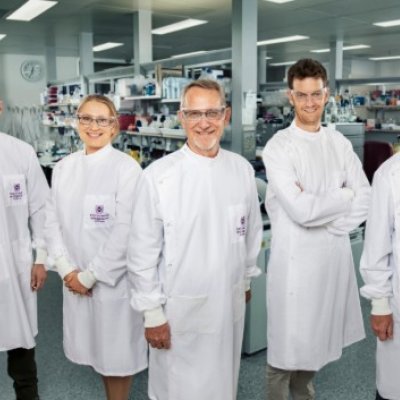 Five scientists in white lab coats stand in a row.