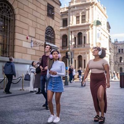 Three people standing in the middle of a city wearing headphones and looking up