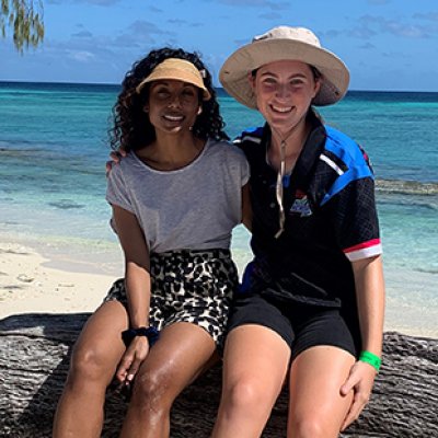 Dr Sonia Shah and Cadence Taylor sitting on a log on a beach with the ocean in the background