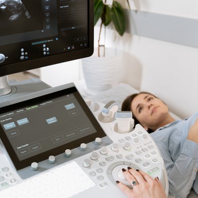 A woman lying on a bed undergoing a sonogram with a concerned look on her face