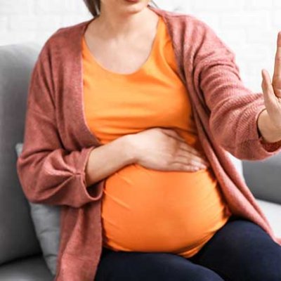 pregnant woman holding up her hand to an alcoholic beverage