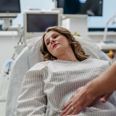 Woman in hospital bed wearing a hospital gown with her abdomen being examined. 