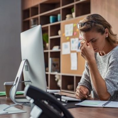 A woman in a grey sweater looking frustratingly at her computer 