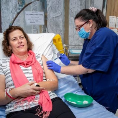 A woman lies in a hospital bed as a nurse prepares to give her a vaccine by needle. 