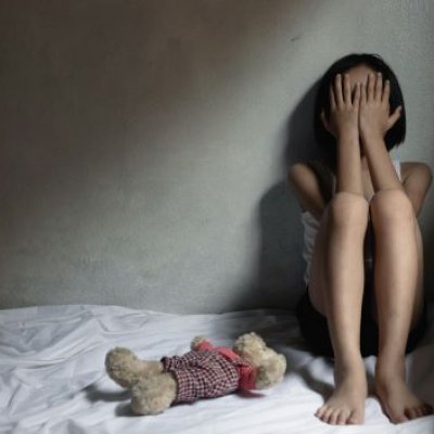 A young child sitting on a bed with their head in their hands, looking upset