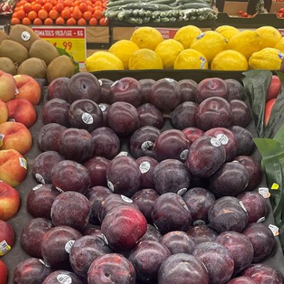 a tray of plums among other fruit in a supermarket