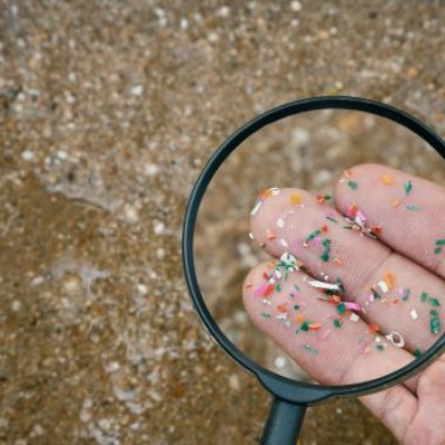 Fingers holding microplastics shown through a magnifying glass