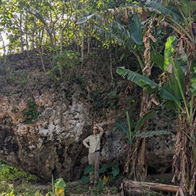 a man stands in front of a large rock holding a measuring tape