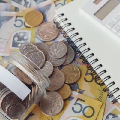 A notebook and calculator sit next to bank notes and a jar of coins
