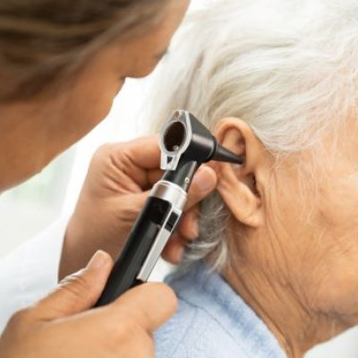 A audiologist inserting a stethoscope into a elderly patient's ear
