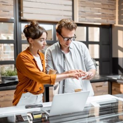 A man and woman in a workplace stand next to a laptop