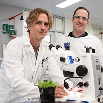 two men in white coats stand by a microscope with a light