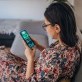 A woman sits on a couch looking at a phone showing a sports betting app