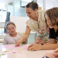 A teacher at a table with two students in a classroom.