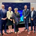 Five people, including Professor Deborah Terry and Prof Tracey Bunda standing in a row in front of a stage and lectern.