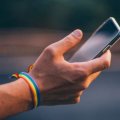  A hand wearing a rainbow bracelet holds a mobile phone.