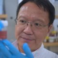 Researcher in a lab examining a container of sample nanoparticles used in breast cancer research. 
