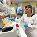 Professor Ranjeny Thomas wearing a lab coat and safety glasses working in the lab