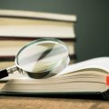A stack of novels with a magnifying glass.