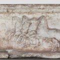 A stone carving featuring a chariot being pulled by four horses.