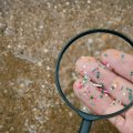 Fingers holding microplastics shown through a magnifying glass