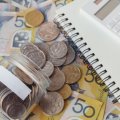 A notebook and calculator sit next to bank notes and a jar of coins