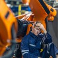A tired worker sits in front of machinery with his hand on his head