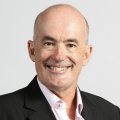 A man in a suit jacket and shirt smiles broadly.