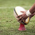 Hands holding a rugby ball on a kicking tee. 