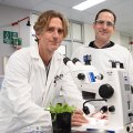 two men in white coats stand by a microscope with a light