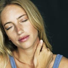 A woman holds her neck in pain with her right hand.