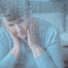 Senior aged woman gazing out of a window through water droplets covering glass