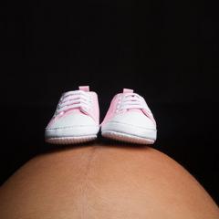 a pregnant stomach with baby shoes balancing on it