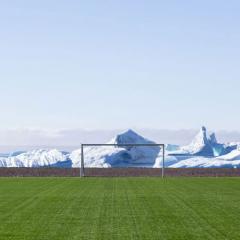 Green soccer/football field and goal post with snowy peaks in the background