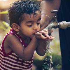 A child drinking water from an outside tap
