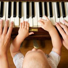 A baby sitting on an adults lap playing a piano 