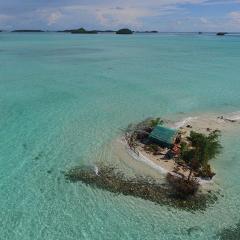 A house on a small island/sand bank with the blue ocean surrounding it.