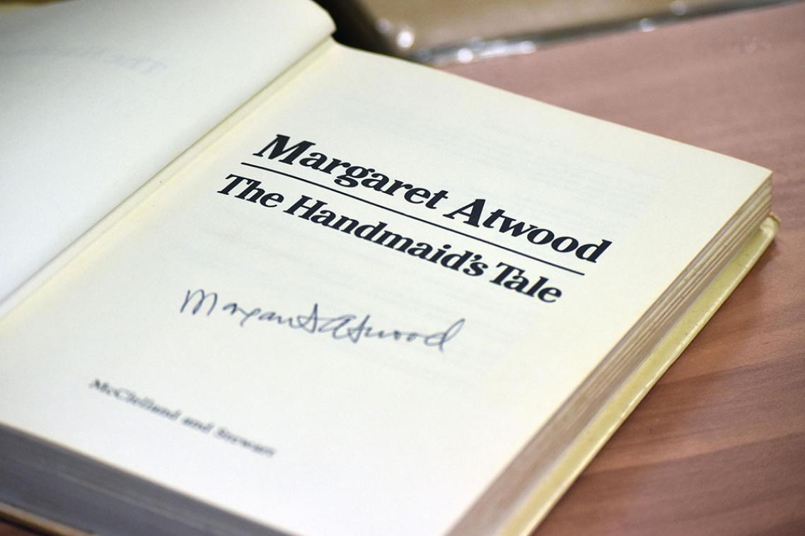 An open book with the text The Handmaid's Tale, with a signature at the bottom. 