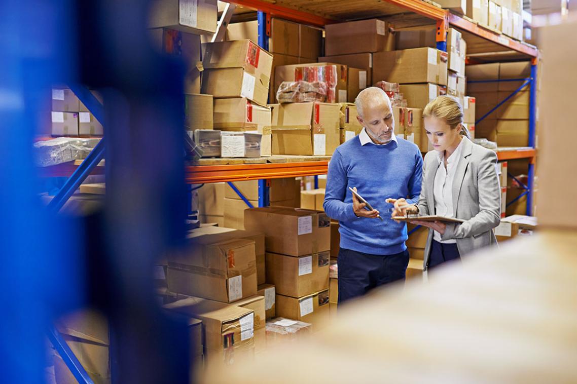 Two people standing in a warehouse looking at a clipboard 