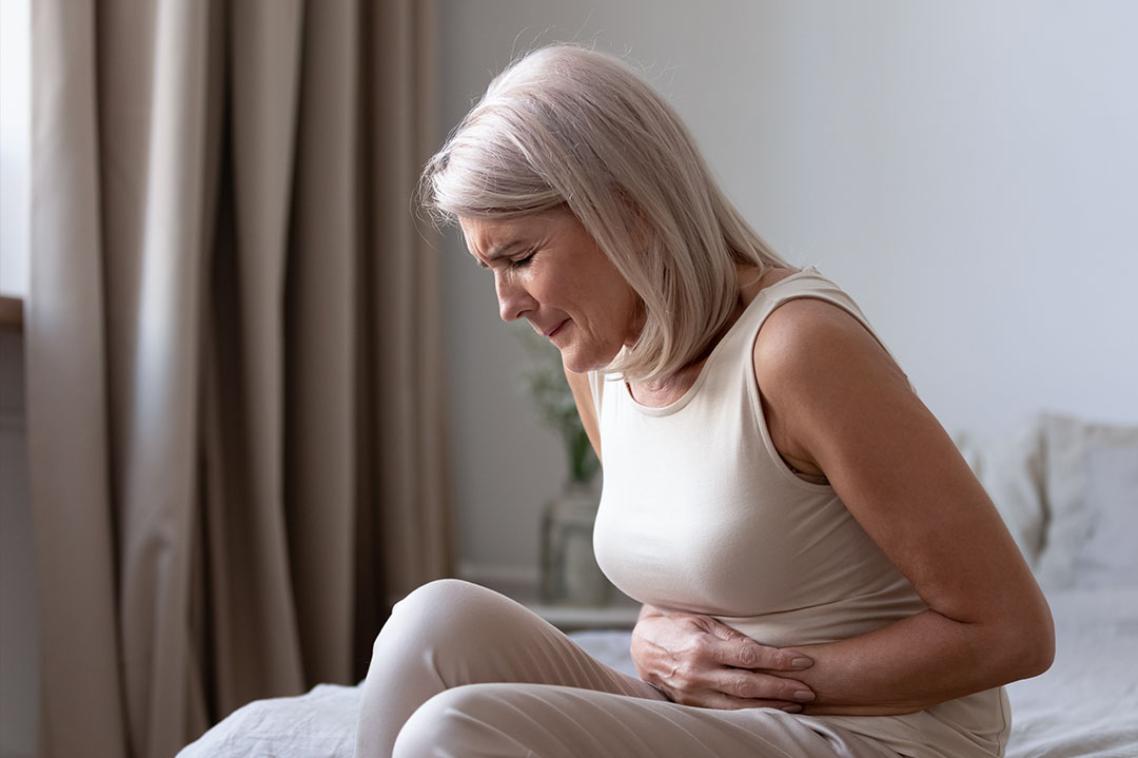 An older woman sitting in bed, bent over in pain