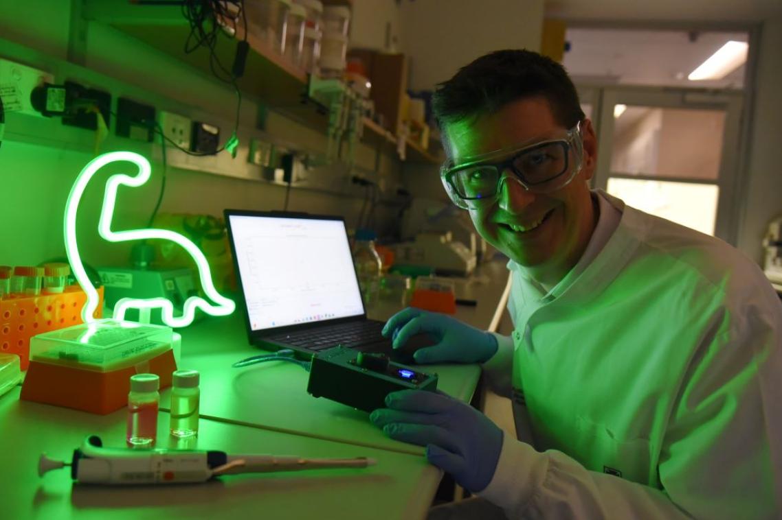 A dinosaur shaped light on a lab bench, a man working on something in a lab coat and glasses