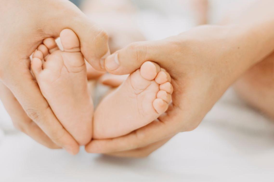 A set of hands holding babies feet in a heart shape