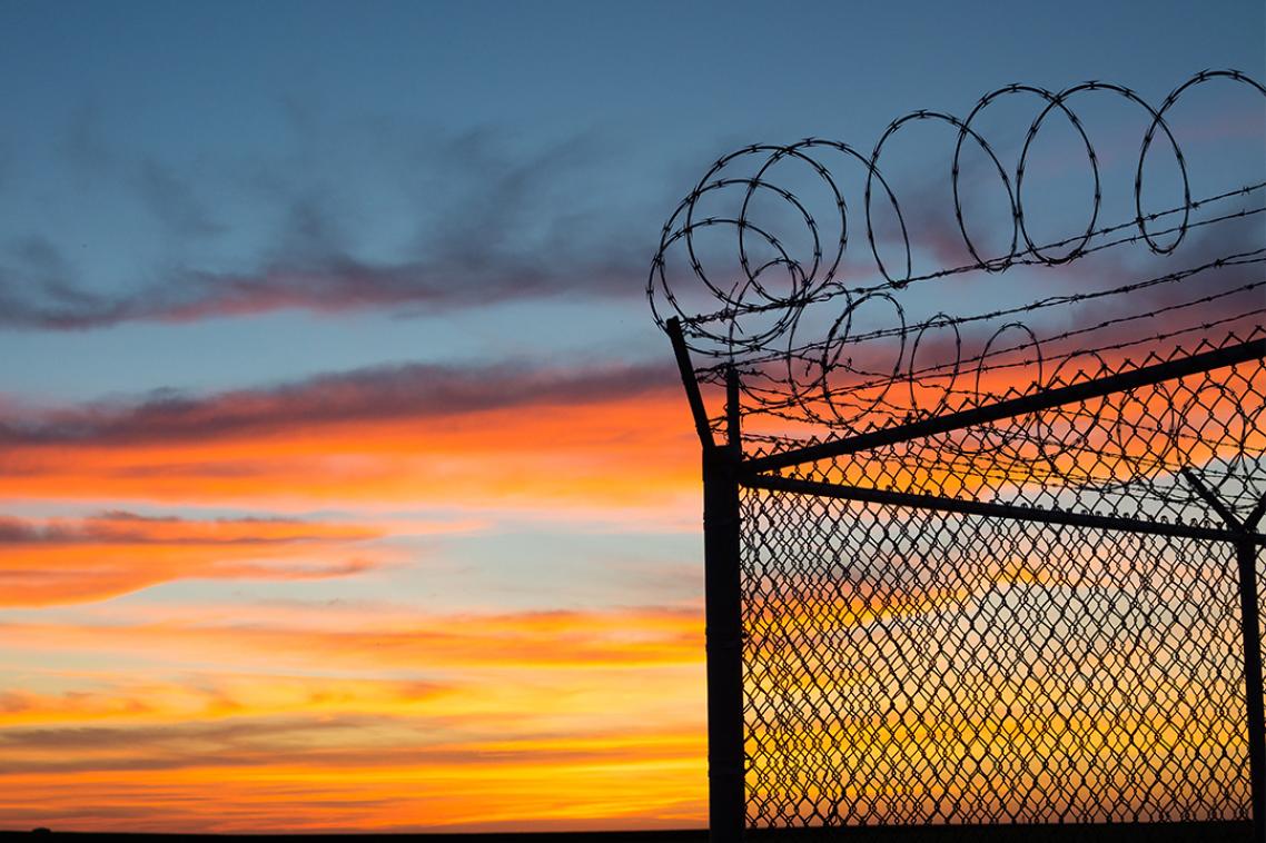 The outer fence of a prison with barbed wire at sunset.